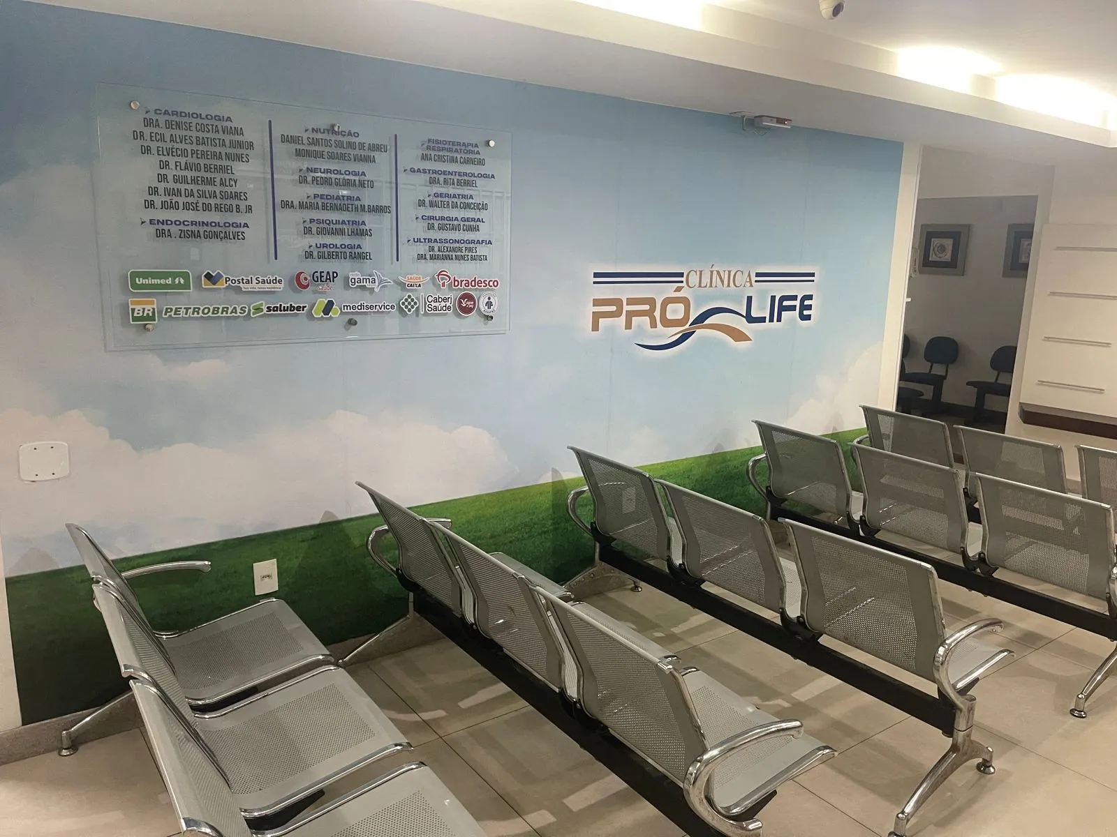 Sala de espera da Clínica Pró Life, com o painel de especialidades e o logo na parede